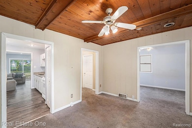 Unfurnished living room featuring dark colored carpet, a wooden ceiling with exposed beams, and ceiling fan
