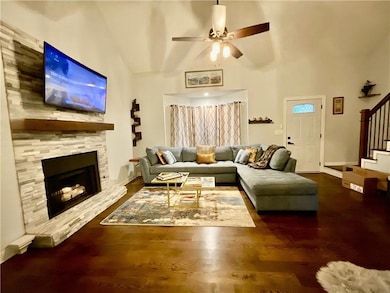 Living room featuring a stone fireplace, wood finished floors, ceiling fan, and stairway