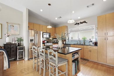 Kitchen with stainless steel appliances, a kitchen breakfast bar, decorative light fixtures, light wood-style floors, and a kitchen island