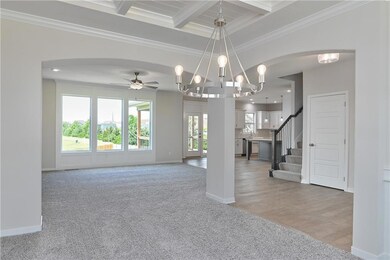 Unfurnished living room with light carpet, beamed ceiling, arched walkways, ornamental molding, and baseboards