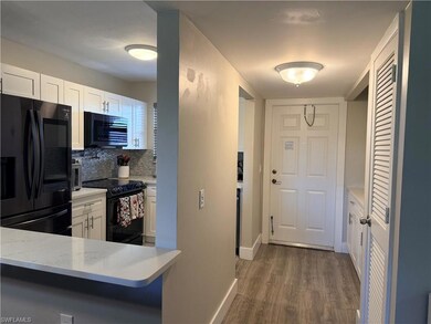 Kitchen featuring black appliances, white cabinets, light stone counters, dark wood finished floors, and backsplash