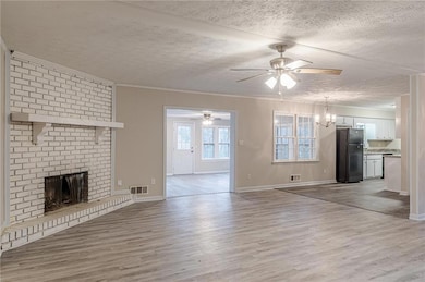 Unfurnished living room with a ceiling fan, light wood-type flooring, a brick fireplace, a textured ceiling, and ornamental molding