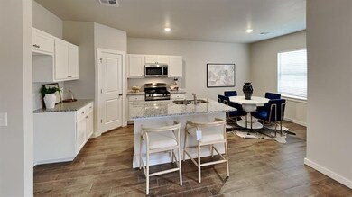 Kitchen featuring stainless steel appliances, dark wood-type flooring, light stone counters, white cabinets, and a kitchen island with sink