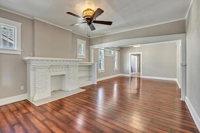 Living room with hardwood / wood-style floors, ceiling fan, crown molding, and a fireplace