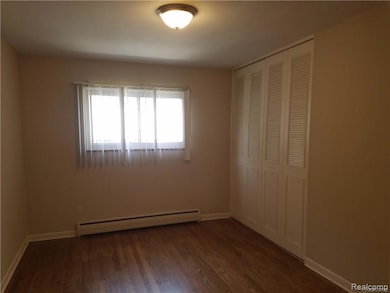 Unfurnished bedroom with a baseboard heating unit, a closet, and dark wood-type flooring