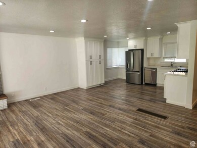 Kitchen featuring a textured ceiling, stainless steel appliances, white cabinetry, light countertops, and dark wood-style floors