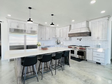 Kitchen featuring concrete flooring, custom range hood, high end appliances, and backsplash