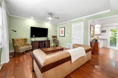 Living room with wood finished floors, a ceiling fan, crown molding, and recessed lighting