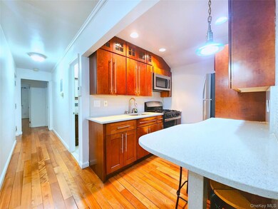 Kitchen with stainless steel appliances, hanging light fixtures, brown cabinetry, light wood-type flooring, and light stone countertops