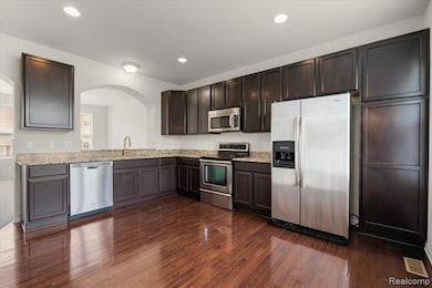 Kitchen featuring stainless steel appliances, dark wood-style flooring, recessed lighting, light stone countertops, and dark brown cabinetry