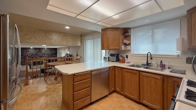 Kitchen featuring appliances with stainless steel finishes, brown cabinetry, light countertops, and a peninsula