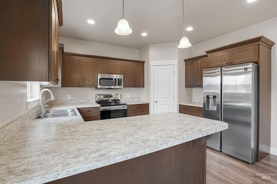 Kitchen featuring appliances with stainless steel finishes, a peninsula, light countertops, pendant lighting, and light wood-style flooring