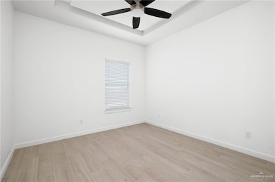 Empty room featuring a raised ceiling, light wood-style flooring, and ceiling fan