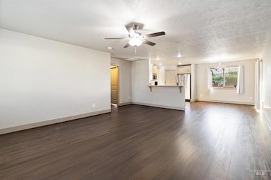 Unfurnished living room with dark wood-style flooring, ceiling fan, and a textured ceiling