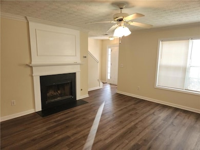 Unfurnished living room with dark wood-style flooring, a textured ceiling, ornamental molding, a fireplace with flush hearth, and ceiling fan