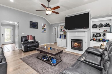 Living room with light hardwood / wood-style flooring, a tiled fireplace, crown molding, lofted ceiling, and ceiling fan