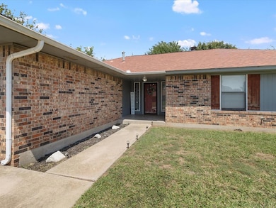 Entrance to property with a lawn, brick siding, and roof with shingles