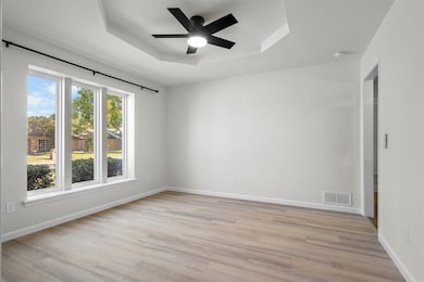 Unfurnished room featuring a tray ceiling, light wood-style floors, and ceiling fan