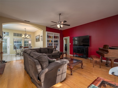Living area featuring arched walkways, a ceiling fan, a chandelier, and light wood-style flooring