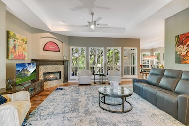 Living room featuring a tray ceiling, wood finished floors, a ceiling fan, and a fireplace