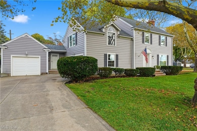 View of front of property featuring a front lawn, concrete driveway, a chimney, an attached garage, and roof with shingles