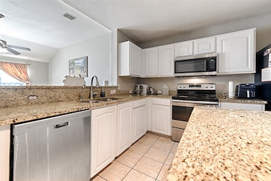 Kitchen featuring light stone countertops, appliances with stainless steel finishes, light tile patterned floors, vaulted ceiling, and a textured ceiling