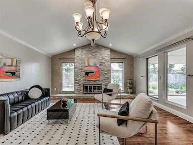 Living area featuring wood finished floors, vaulted ceiling, a stone fireplace, plenty of natural light, and a chandelier