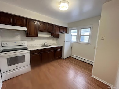 Kitchen featuring white appliances, dark brown cabinets, light countertops, a baseboard radiator, and ventilation hood