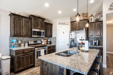 Kitchen featuring appliances with stainless steel finishes, light wood-type flooring, dark brown cabinetry, vaulted ceiling, and a breakfast bar area