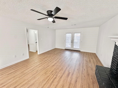 Unfurnished living room with light wood-style floors, a textured ceiling, a ceiling fan, french doors, and a brick fireplace