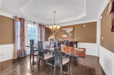Dining space with a tray ceiling, a chandelier, wainscoting, crown molding, and a decorative wall