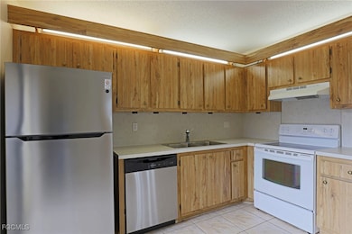 Kitchen with appliances with stainless steel finishes, light countertops, light tile patterned floors, under cabinet range hood, and a textured ceiling