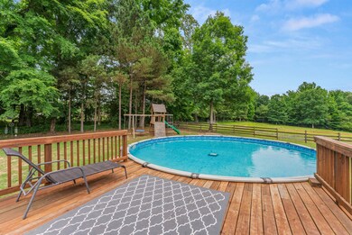 Outdoor pool with a playground, a deck, and view of wooded area
