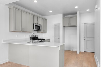 Kitchen featuring gray cabinets, a peninsula, appliances with stainless steel finishes, light wood finished floors, and light countertops