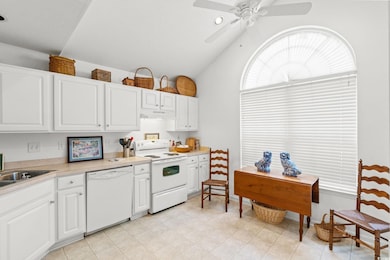 Kitchen with white cabinetry, white appliances, light countertops, lofted ceiling, and under cabinet range hood