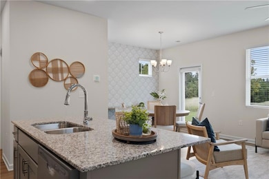 Kitchen featuring light stone countertops, hanging light fixtures, a kitchen island with sink, and stainless steel dishwasher