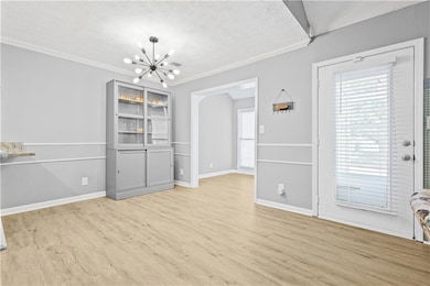 Unfurnished dining area with a chandelier, light wood-style flooring, baseboards, and ornamental molding