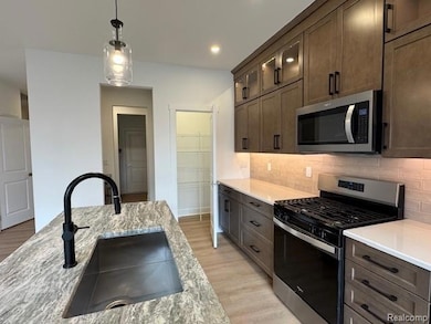 Kitchen featuring appliances with stainless steel finishes, light wood finished floors, decorative light fixtures, light stone countertops, and dark brown cabinets