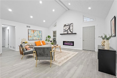 Living area with beamed ceiling, high vaulted ceiling, light wood-style floors, a glass covered fireplace, and recessed lighting