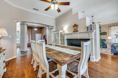 Dining room with decorative columns, ceiling fan, a fireplace, crown molding, and wood finished floors