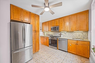 Kitchen featuring stainless steel appliances, a sink, decorative backsplash, a ceiling fan, and brown cabinets