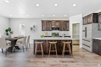 Kitchen featuring light wood-style floors, dark brown cabinets, recessed lighting, light countertops, and a breakfast bar area