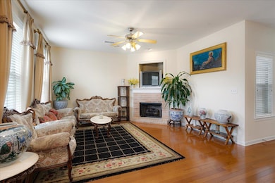 Living room featuring baseboards, a ceiling fan, wood-type flooring, and a brick fireplace