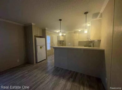 Kitchen with dark wood-style floors, freestanding refrigerator, a peninsula, a textured ceiling, and hanging light fixtures