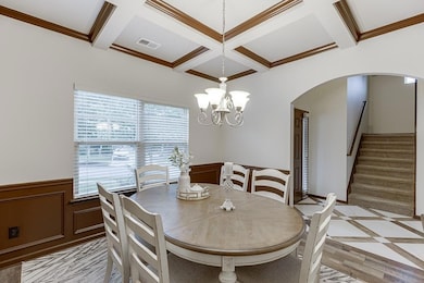 Dining room featuring arched walkways, coffered ceiling, plenty of natural light, wainscoting, and stairs