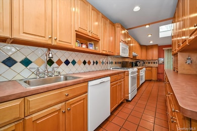 Kitchen with light tile patterned floors, white appliances, a skylight, light countertops, and decorative backsplash
