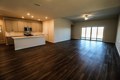 Kitchen featuring dark wood-type flooring, an island with sink, ceiling fan, gray cabinets, and stove