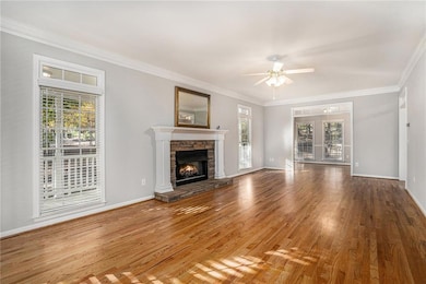 Unfurnished living room with ornamental molding, wood finished floors, ceiling fan, and a fireplace