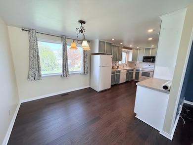 Kitchen featuring light countertops, white appliances, tasteful backsplash, dark wood-type flooring, and gray cabinets