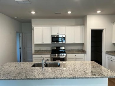 Kitchen featuring appliances with stainless steel finishes, white cabinetry, light stone countertops, and recessed lighting